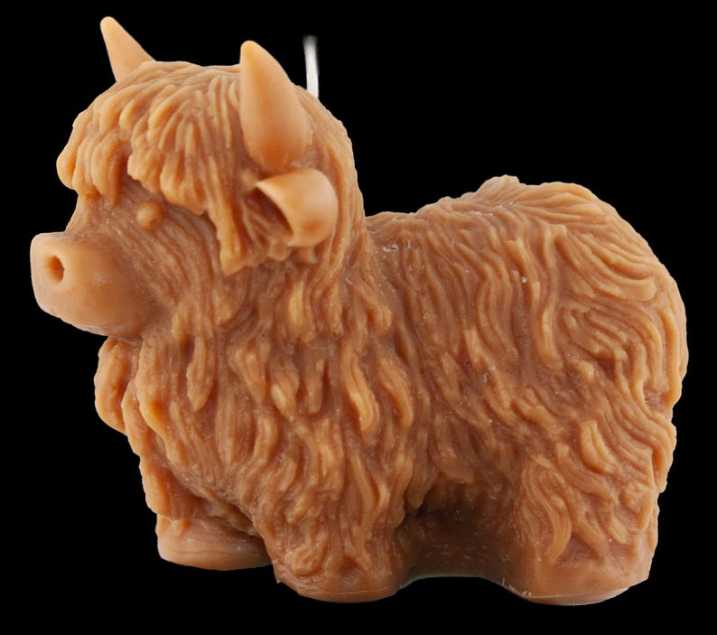 May include: A brown Highland cow figurine with detailed fur texture, horns, and a small tail. The figurine is a light brown color and is set against a black background. The cow is in a standing position.