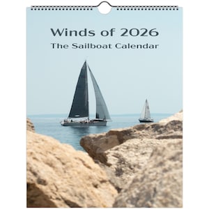 Puede incluir: Un calendario titulado "Winds of 2026, The Sailboat Calendar" presenta dos veleros en el agua. El velero más grande tiene una vela gris oscura, y el más pequeño tiene una vela blanca. En primer plano, rocas de color marrón claro.