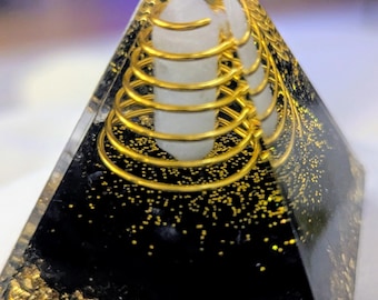 May include: A black crystal pyramid with gold glitter and a clear quartz crystal inside. A gold wire coil surrounds the quartz crystal.