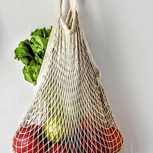 May include: A white mesh produce bag hanging on a wooden hook, filled with red and green apples.