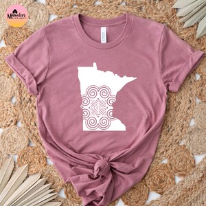 May include: A mauve t-shirt with a white outline of the state of Minnesota with a white mandala design inside the state outline.