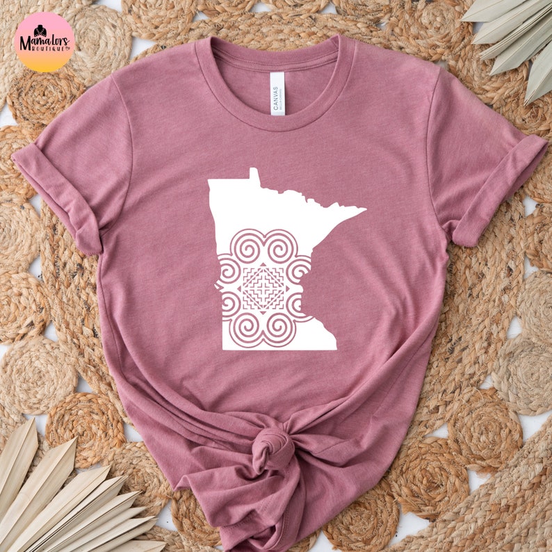 May include: A mauve t-shirt with a white outline of the state of Minnesota with a white mandala design inside the state outline.