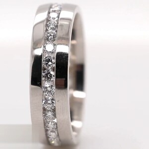 May include: A silver ring with a channel setting of small, round, clear gemstones. The ring has a flat, brushed metal band with a polished edge. The ring is a jewelry item.