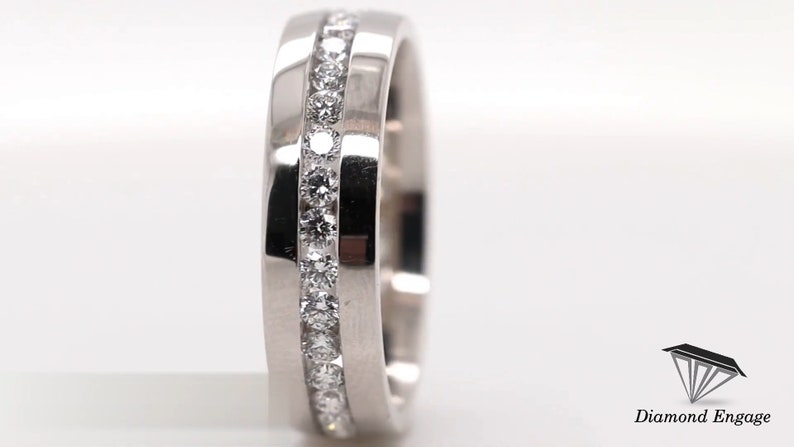 May include: A silver ring with a channel setting of small, round, clear gemstones. The ring has a flat, brushed metal band with a polished edge. The ring is a jewelry item.
