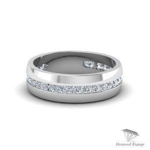 May include: A silver-colored ring with a channel setting of small, clear gemstones. The ring has a flat, wide band with a row of gemstones set into the center. The ring is displayed on a white background.