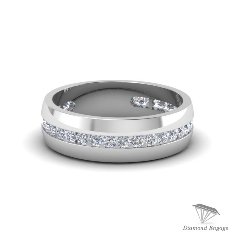 May include: A silver-colored ring with a channel setting of small, clear gemstones. The ring has a flat, wide band with a row of gemstones set into the center. The ring is displayed on a white background.