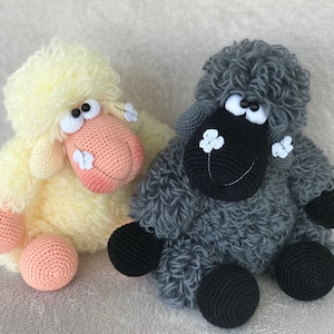 Puede incluir: Dos juguetes de oveja de crochet, uno amarillo y otro gris. Ambas ovejas tienen ojos negros y detalles de flores blancas.