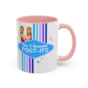 Può includere: Tazza in ceramica bianca con interno e manico rosa. La tazza presenta il testo "Um, I Invented POST-ITS" in un cartello blu in stile retrò. La tazza ha anche un design a strisce verticali colorate e immagini di due donne.
