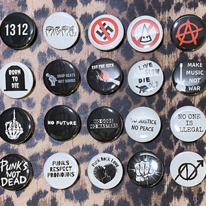 May include: A collection of 16 round black and white buttons with various punk rock themed designs and slogans. The buttons feature slogans such as "No Future", "No Gods No Masters", "Punk's Not Dead", "Live Slow Die Old", and "Make Music Not War".