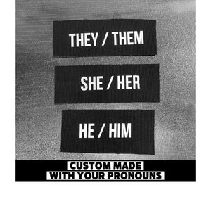 May include: Three black fabric patches with white text. The top patch says "THEY / THEM", the middle patch says "SHE / HER", and the bottom patch says "HE / HIM". Below the patches is the text "CUSTOM MADE WITH YOUR PRONOUNS".