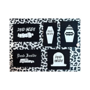 Puede incluir: Cinco parches termoadhesivos negros con texto y gráficos blancos. Los parches presentan el texto "Dead Inside" y varios gráficos, incluyendo un ataúd, una lápida, un coche fúnebre, un frasco y un cuerpo.
