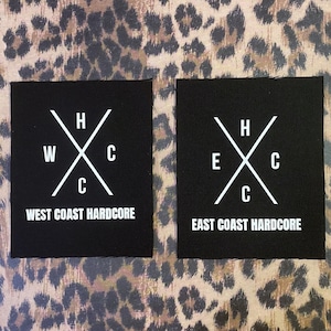 Puede incluir: Dos parches de tela negra con texto blanco y un diseño de cruz blanca. El parche de la izquierda dice "West Coast Hardcore" y el parche de la derecha dice "East Coast Hardcore".