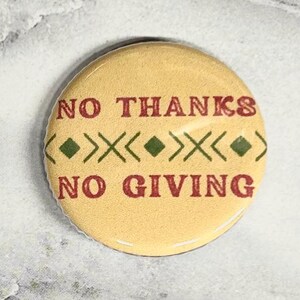 May include: A round, yellow button with the words "NO THANKS" and "NO GIVING" in red, with a green and white geometric design. The button is a fun, decorative accessory.