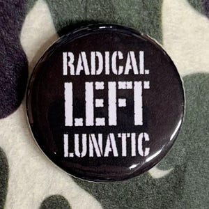 May include: A round, black button with white text that reads "RADICAL LEFT LUNATIC." The button is set against a camouflage pattern background in shades of green, brown, and black. The text is bold and easy to read.