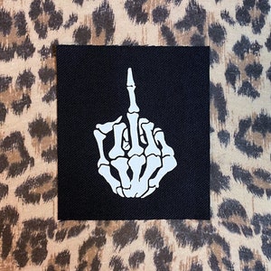 May include: A black fabric patch with a white skeleton hand giving the middle finger.
