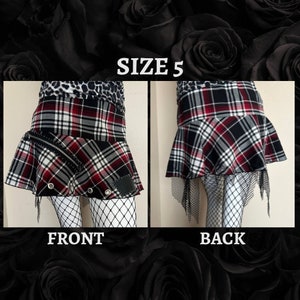 May include: A black, white, and red plaid skirt with a black mesh overlay. The skirt has a zipper detail on the front and a patch on the back. The skirt is size 5.