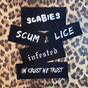 May include: Four black fabric patches with white text. The patches read "SCABIES", "SCUM", "LICE", and "infested". A fifth patch reads "IN CRUST WE TRUST".