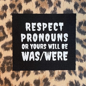 May include: Black fabric patch with white text that reads "Respect Pronouns or Yours Will Be Was/Were".