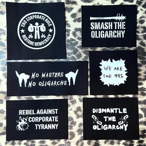 Puede incluir: Seis parches de tela negra con texto blanco y gráficos. Los parches presentan lemas como "End Corporate Rule", "Smash the Oligarchy", "No Masters No Oligarchs", "We Are the 99%", "Rebel Against Corporate Tyranny" y "Dismantle the Oligarchy".