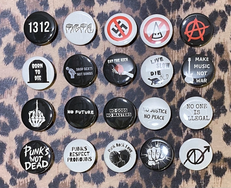 May include: A collection of 16 round black and white buttons with various punk rock themed designs and slogans. The buttons feature slogans such as "No Future", "No Gods No Masters", "Punk's Not Dead", "Live Slow Die Old", and "Make Music Not War".