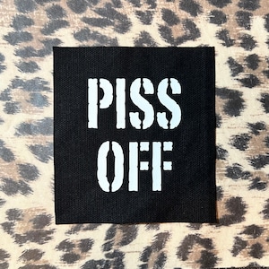 May include: Black fabric patch with white text that reads "PISS OFF" in a stencil font.