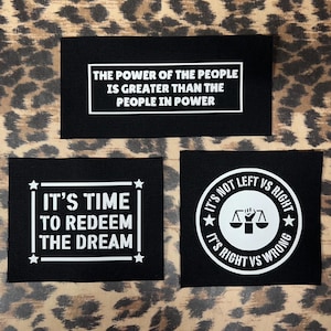 May include: Three black fabric patches with white text and graphics. The top patch reads "The power of the people is greater than the people in power". The middle patch reads "It's time to redeem the dream". The bottom patch has a circle with a scale and a fist inside and the text "It's not left vs right, it's right vs wrong".