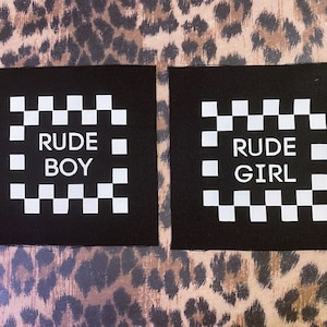 Op de afbeelding: Twee zwarte stoffen patches met witte geruite patronen en de tekst "RUDE BOY" en "RUDE GIRL" in wit.