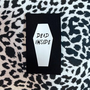 May include: Black fabric patch with a white coffin shape and the text "DEAD INSIDE" inside the coffin.