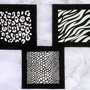 Peut inclure: Trois carrés de tissu noir avec des motifs d'animaux blancs. Les motifs sont un imprimé léopard, un imprimé zèbre et un imprimé peau de serpent.