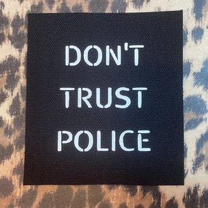 May include: Black patch with white text that reads "DON'T TRUST POLICE".