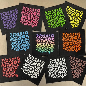 May include: A collection of black fabric squares, each featuring a unique leopard print design in various vibrant colors. The prints include purple, pink, green, yellow, blue, rainbow, orange, red, white, and brown. These squares are ideal for crafting projects.