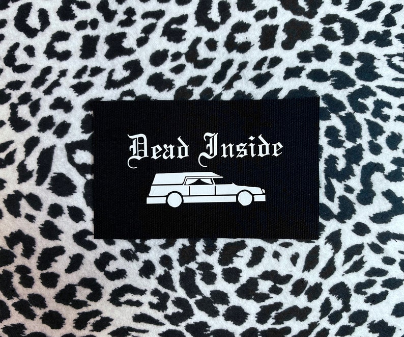 May include: Black patch with white text that reads "Dead Inside" and a white silhouette of a hearse.