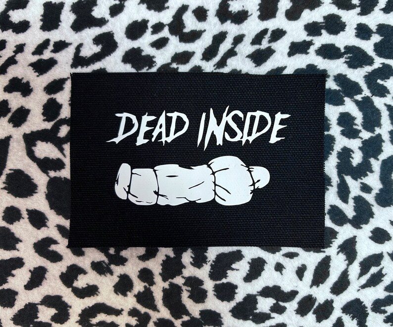 May include: Black fabric patch with white text that reads "DEAD INSIDE" and a white cartoon image of a hand.