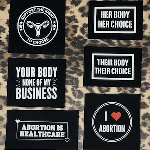 Puede incluir: Un conjunto de nueve parches de tela negra con texto blanco y gráficos. Los parches presentan lemas relacionados con los derechos reproductivos, que incluyen "Apoyar el derecho a elegir", "Su cuerpo, su decisión", "Su cuerpo, su decisión", "Tu cuerpo, no mi asunto", "El aborto es atención médica" y "Me encanta el aborto".