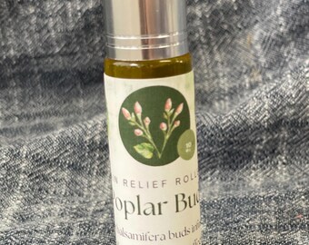 May include: A small glass roller bottle containing a golden-colored oil, topped with a silver metallic cap. The white label features a circular green graphic with pink buds and text that reads Pain Relief Roller, Poplar Buds, and botanicalmaven.com.