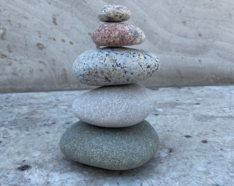 May include: A stack of five smooth, round stones in various shades of gray, brown, and pink, balanced on top of each other.