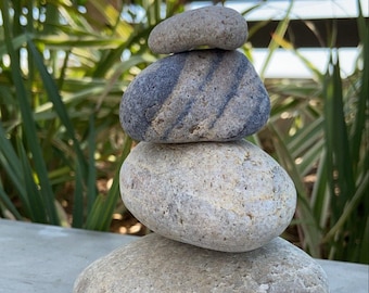 May include: A stack of four gray and white stones balanced on top of each other. The stones are smooth and rounded, and they are arranged in a pyramid shape.