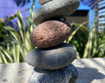 May include: A stack of five smooth, gray, brown, and white stones balanced on top of each other. The stones are arranged in a pyramid shape.