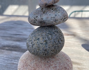 May include: A stack of four smooth, round stones, each with a different color and texture. The stones are balanced on top of each other, creating a zen-like display.