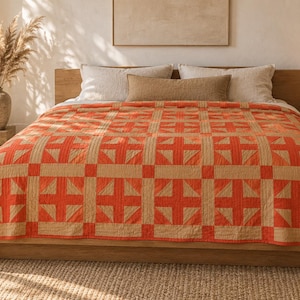 May include: A bed quilt featuring a repeating geometric pattern in vibrant orange and natural beige. The design consists of square blocks with cross-shaped motifs, providing a structured look that covers the entire surface of the bed frame.