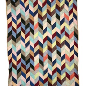 Puede incluir: Una colcha rectangular con un patrón de chevrón repetitivo compuesto por varios parches de tela en tonos burdeos, azul marino, azul claro, bronceado, negro, rosa y verde lima, terminada con un borde de tela color bronceado.