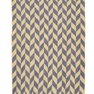 May include: A large, rectangular blanket with a repeating chevron pattern. The design features alternating rows of navy blue and cream-colored chevrons. The blanket is made of a soft, textured fabric and has a stitched border.