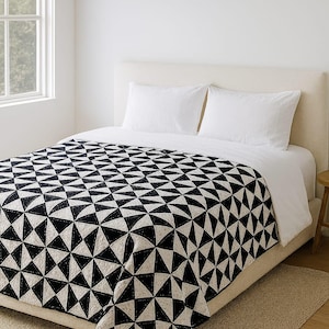 Puede incluir: Un edredón con estampado geométrico en blanco y negro sobre una cama con almohadas blancas y un edredón blanco. El edredón presenta un diseño de triángulo repetido. La cama está en una habitación luminosa con una ventana.