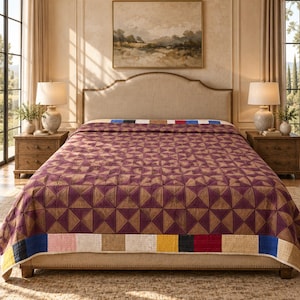 Op de afbeelding: Een rechthoekige sprei met een herhalend geometrisch patroon van donkerpaarse en beige driehoeken. De sprei is afgewerkt met een rand van afwisselende effen gekleurde vierkanten in wit, beige, geel, zwart, rood en blauw langs de randen.