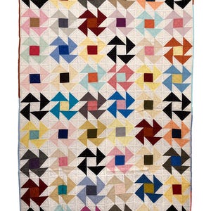 May include: A rectangular quilt featuring a repeating pinwheel pattern composed of various solid-colored fabric squares. The design includes a white background with small, evenly spaced stitching throughout, creating a textured grid effect.