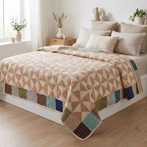 Peut inclure: Un lit avec une courtepointe à motifs géométriques dans des tons de beige et de crème. La courtepointe présente une bordure patchwork avec des carrés de différentes couleurs. Des oreillers beiges et un couvre-lit neutre complètent le décor de la chambre.