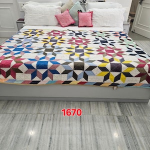 May include: A bed with a colorful quilt featuring a geometric star pattern in shades of blue, pink, yellow, and brown. The bed is made with white pillows and pink accent pillows. The number "1670" is visible in the image.