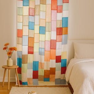 May include: A vibrant patchwork curtain featuring a grid of rectangular fabric pieces in shades of red, blue, orange, and white. The curtain hangs in front of a bed with white bedding. A small wooden table holds a vase of orange flowers.