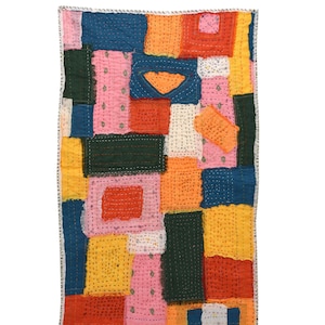 Puede incluir: Una pieza textil rectangular que presenta un mosaico de retazos de tela multicolor en tonos rosa, naranja, amarillo, verde oscuro y azul. Las secciones de tela están unidas con costuras visibles de hilo blanco por toda la pieza.