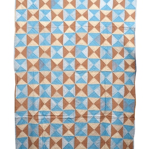 May include: A large, rectangular quilt with a geometric pattern. The design features alternating squares of light blue, beige, and brown triangles. The quilt is made of fabric and has a stitched texture.